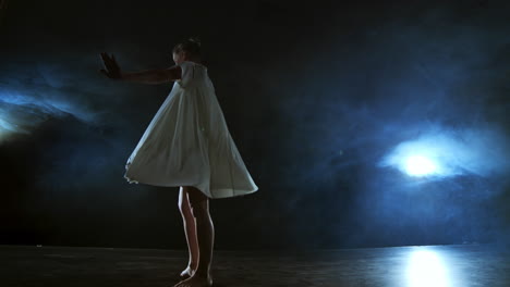 A-woman-in-a-white-dress-is-dancing-on-the-stage-the-dramatic-dances-of-modern-ballet.-A-ballet-dancer-moves-plastic-performing-modern-choreography-in-smoke.